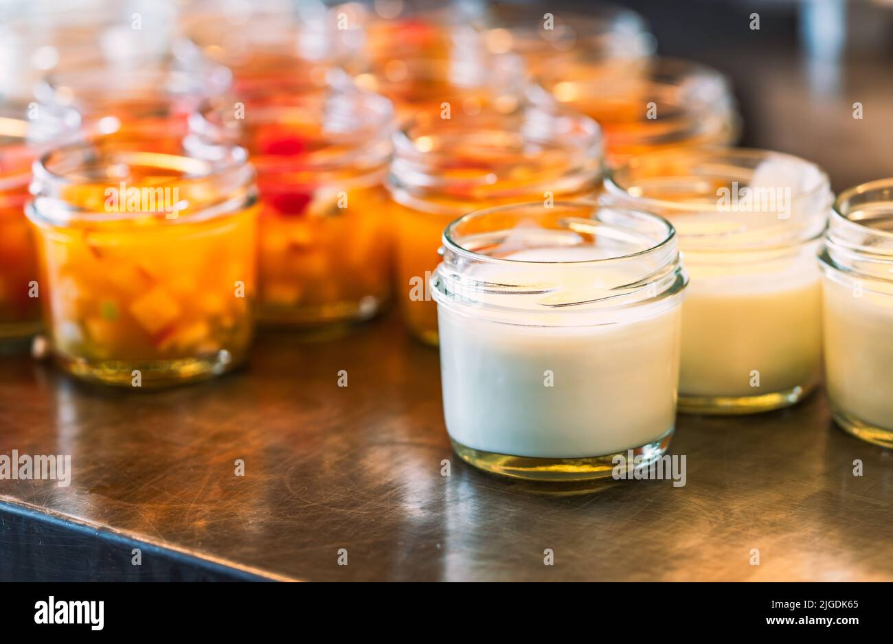 Homemade plain yogurt in small bottle glass on stainless steel shelf with blurred background of fruit salad in small bottle glass, close up image with Stock Photo