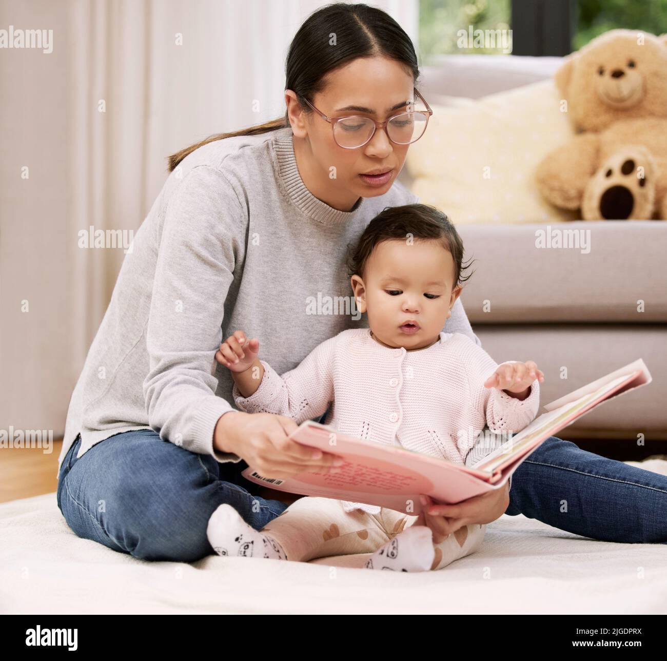With every newborn baby, a little sun rises. Shot a mother reading a book to her baby at home. Stock Photo