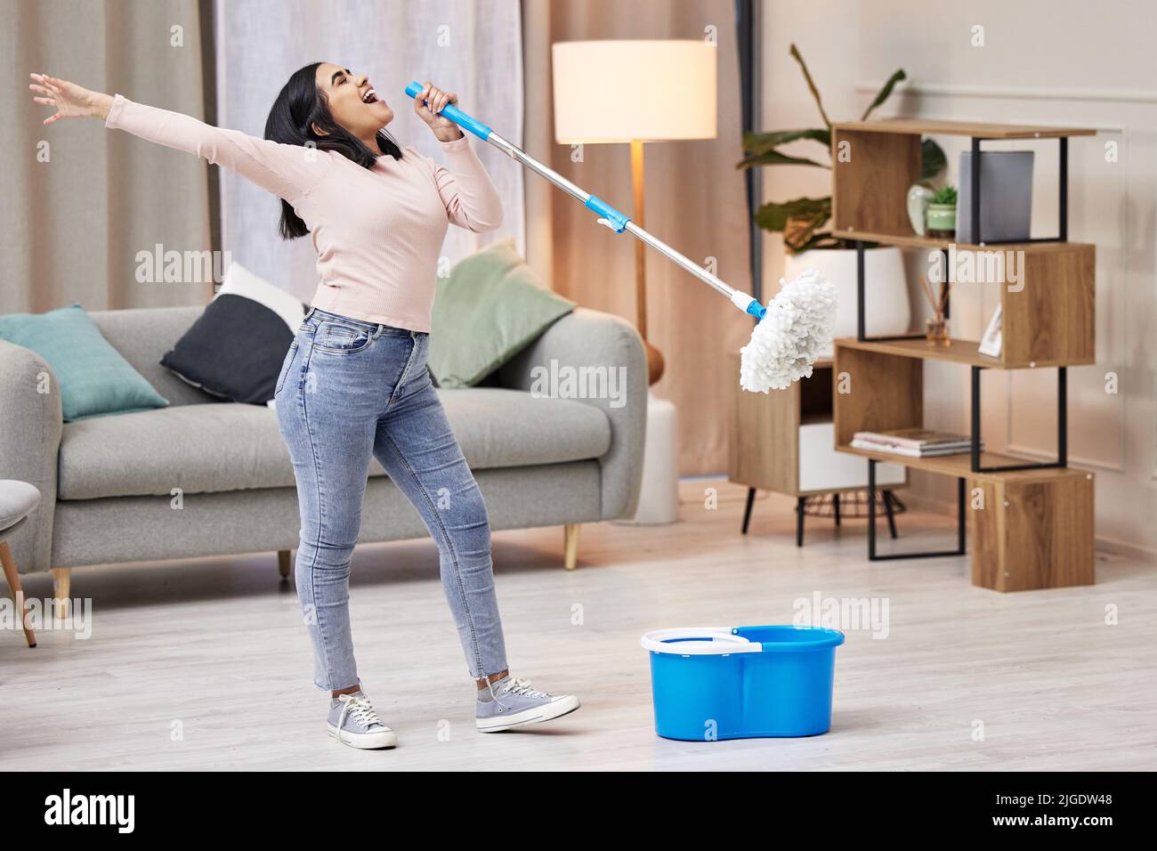 Time for my solo. a young woman singing while mopping the floors at home. Stock Photo