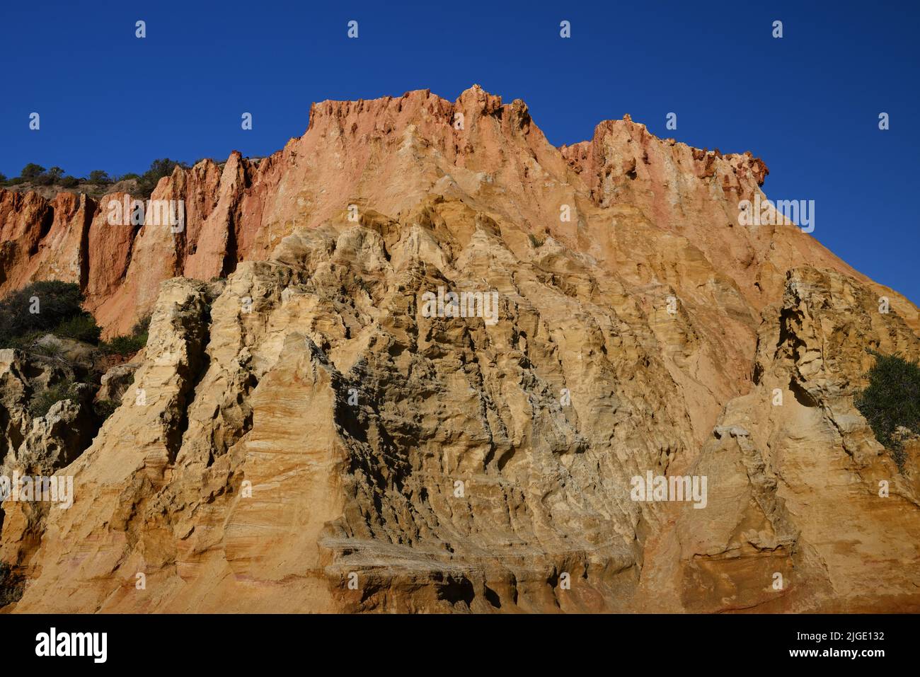 View of the rugged reddish sandstone cliff face at Red Bluff, with blue sky in the background Stock Photo