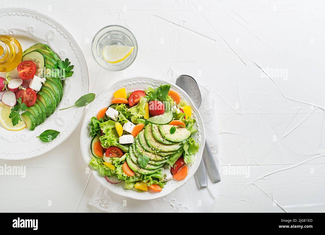 Healthy green salad with avocado, feta cheese and fresh vegetables on white background Stock Photo