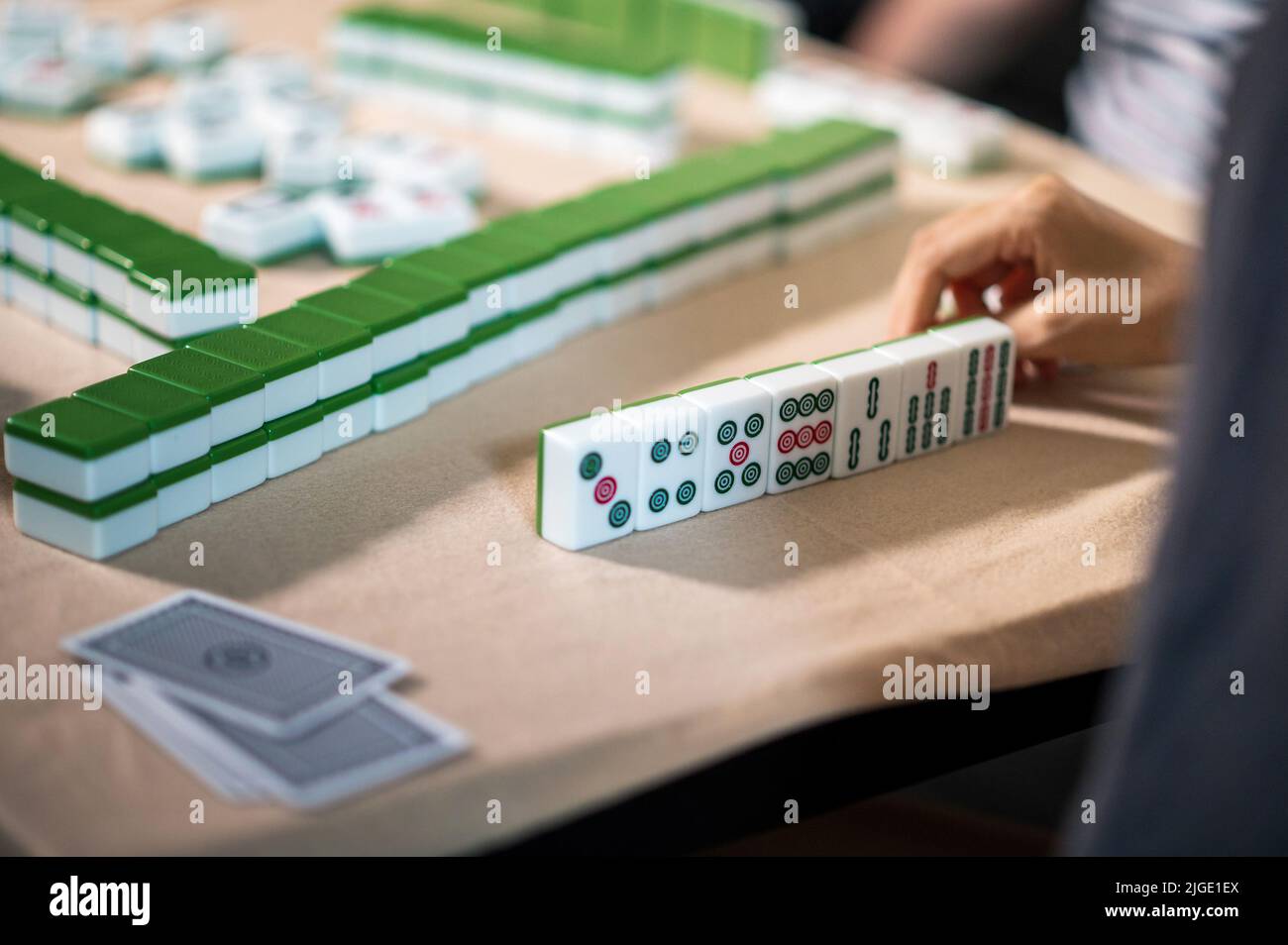 Female friends playing mahjong traditional Chinese board game at home. Translation: Tiles text shows Chinese characters for numbers from 1 to 9 and si Stock Photo