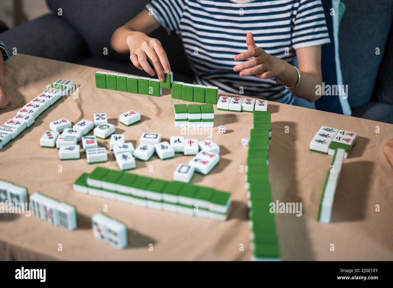 Female friends playing mahjong traditional Chinese board game at home. Translation: Tiles text shows Chinese characters for numbers from 1 to 9 and si Stock Photo