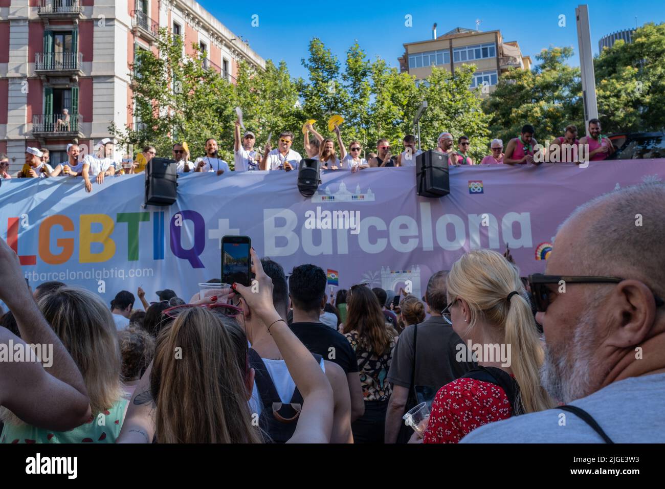 Barcelona, Spain - June 25, 2022: People watching the Pride parade. Rear view of a woman taking a photo as a float with the acronym LGBTIQ passes by. Stock Photo