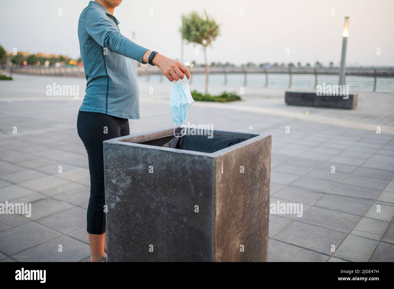 Unrecognizable pregnant woman throwing a used surgical medical face mask in the garbage bin outdoors Stock Photo