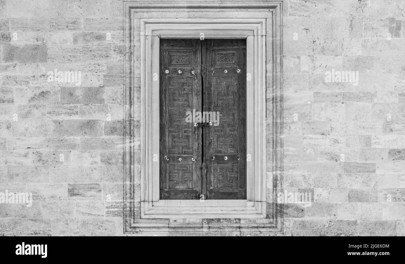 A stone wall with a large window and a wooden pane in black and white Stock Photo