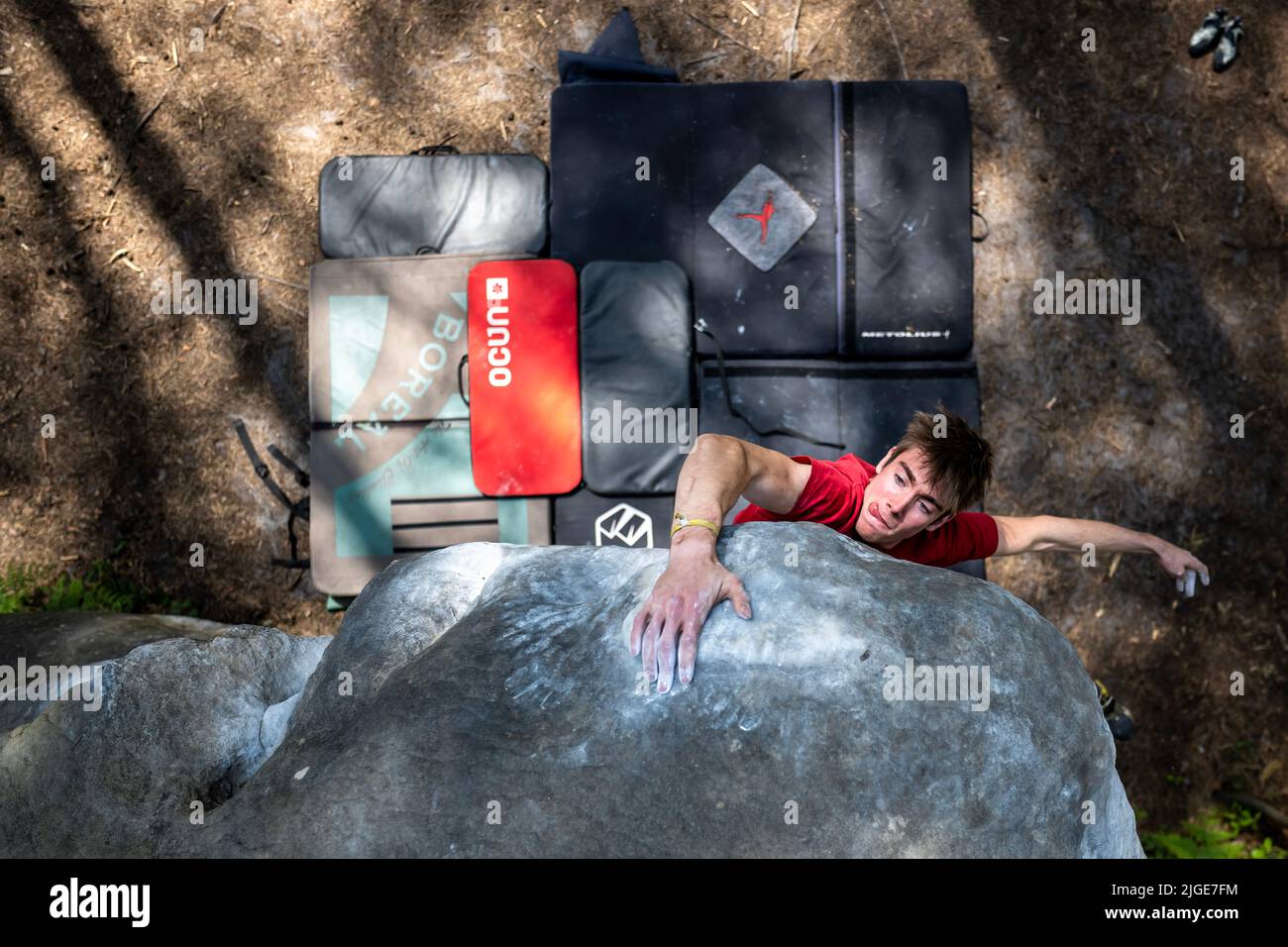 Athletic young man is jumping for top hold in famous and hard dyno boulder problem called 'Cannon Ball -7b'. Fontainbleau, France, Europe. Stock Photo