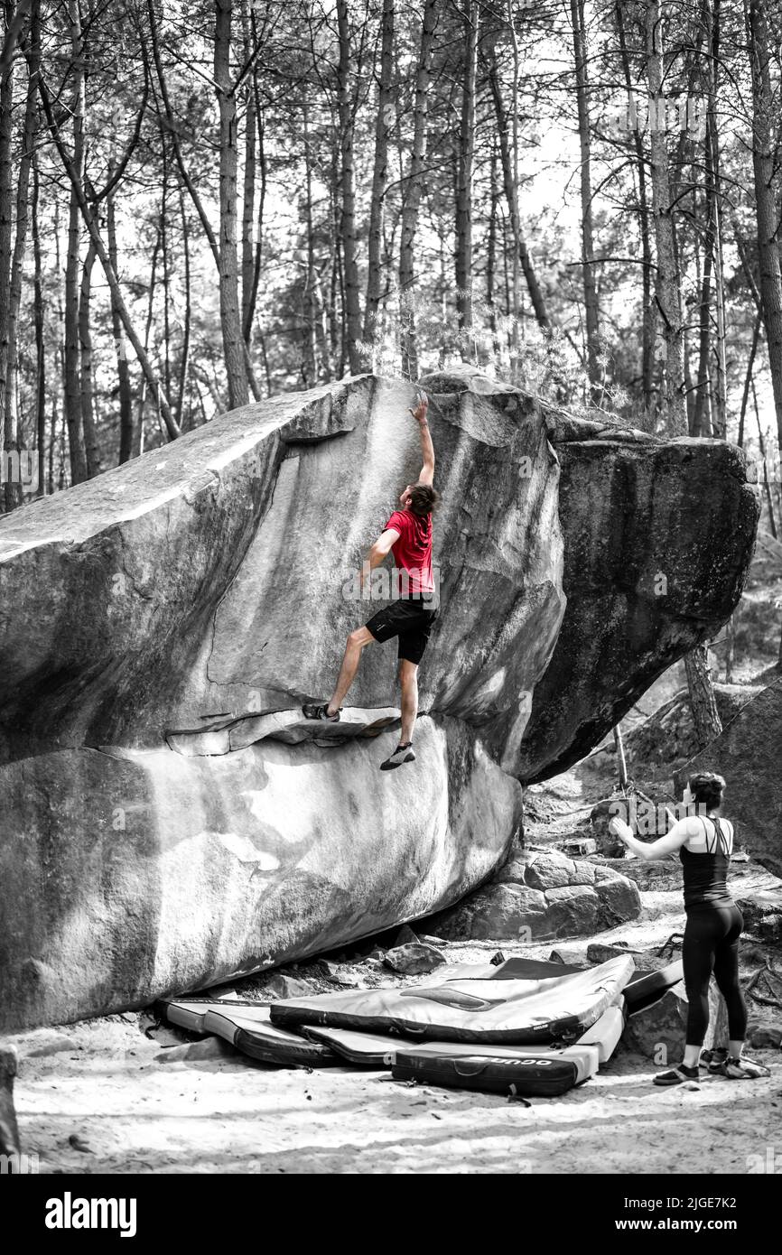 Athletic young man is jumping for top hold in famous and hard dyno boulder problem called 'Rainbow Rocket - 8a'. Fontainbleau, France, Europe. Stock Photo