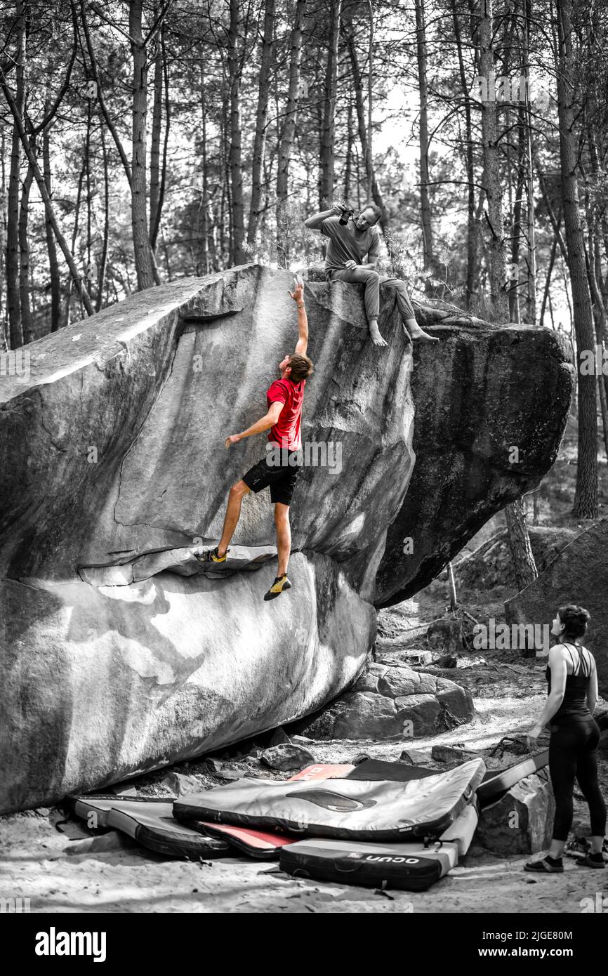 Athletic young man is jumping for top hold in famous and hard dyno boulder problem called 'Rainbow Rocket - 8a'. Fontainbleau, France, Europe. Stock Photo