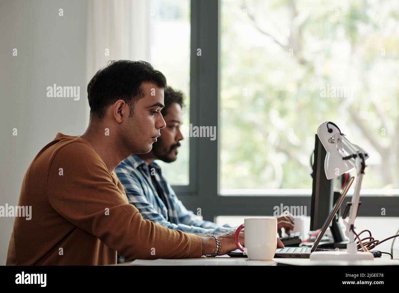 Concentrated young Indian software engineer working on laptop at his office desk Stock Photo