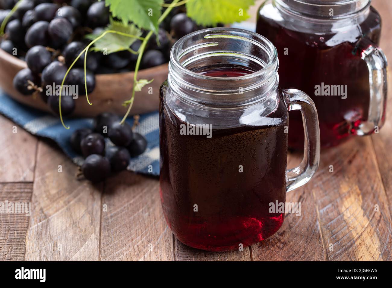 Glass of grape juice and bowl of blsck grapes on a rustic wooden table ...