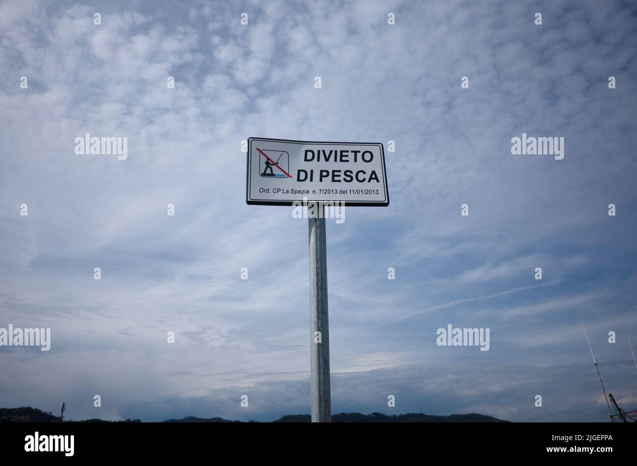 White plate against cloudy sky that says Divieto di Pesca means Fishing prohibited in Italian. Fishing prohibited sign on pier, La Spezia, Liguria Stock Photo