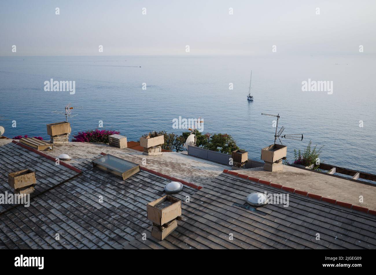 Tiled roofs of Italian houses on Mediterranean coast. Panorama of  Ligurian Sea from roof of house. Landscape with calm water and yacht Stock Photo