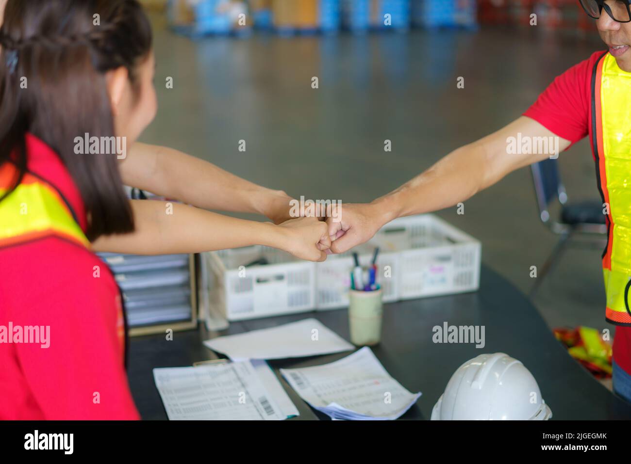 Unity and teamwork concept. Asian worker team standing together and punch their hand before working in warehouse. Stock Photo
