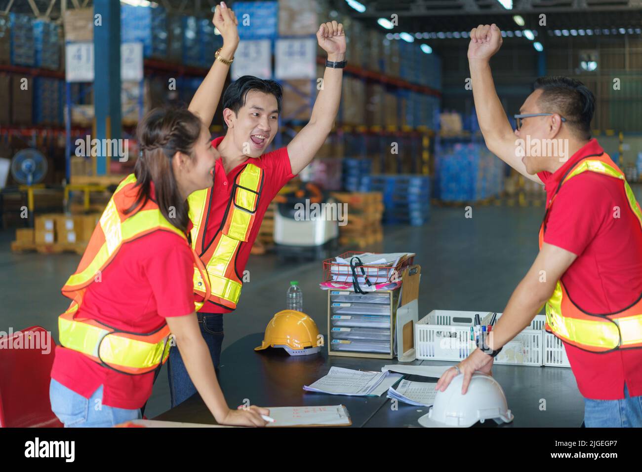 Unity and teamwork concept. Asian worker team standing together and raise their hand before working in warehouse. Stock Photo
