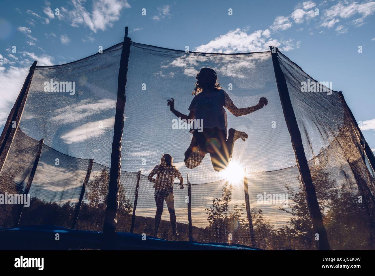Two happy female kids jumping inside a trampoline in Poland on a bright ...