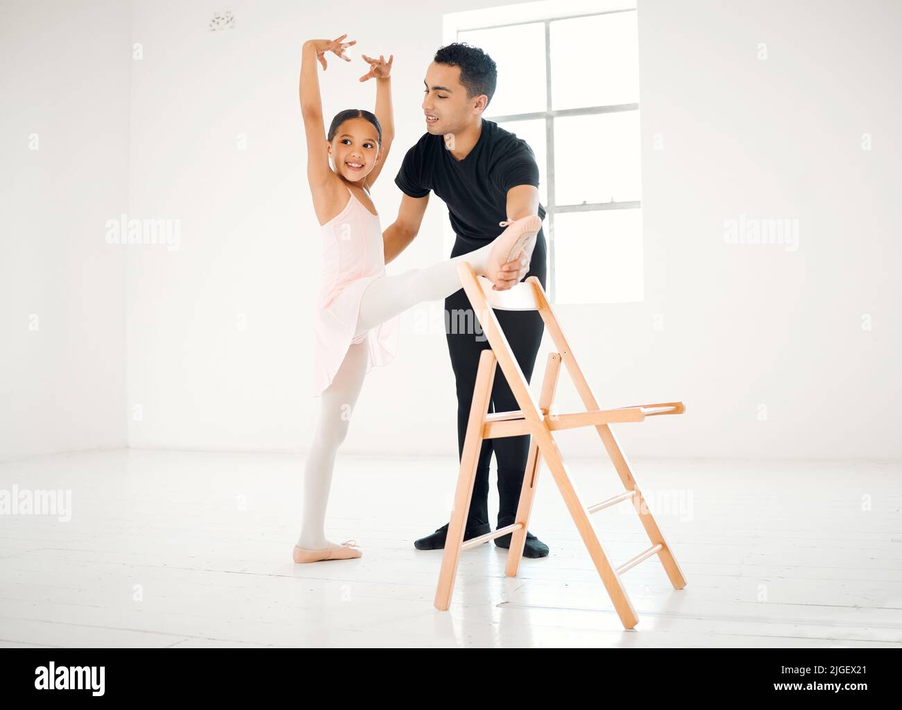 She always looks forward to her weekly ballet lessons. a ballet teacher assisting a student with her position in a dance studio. Stock Photo