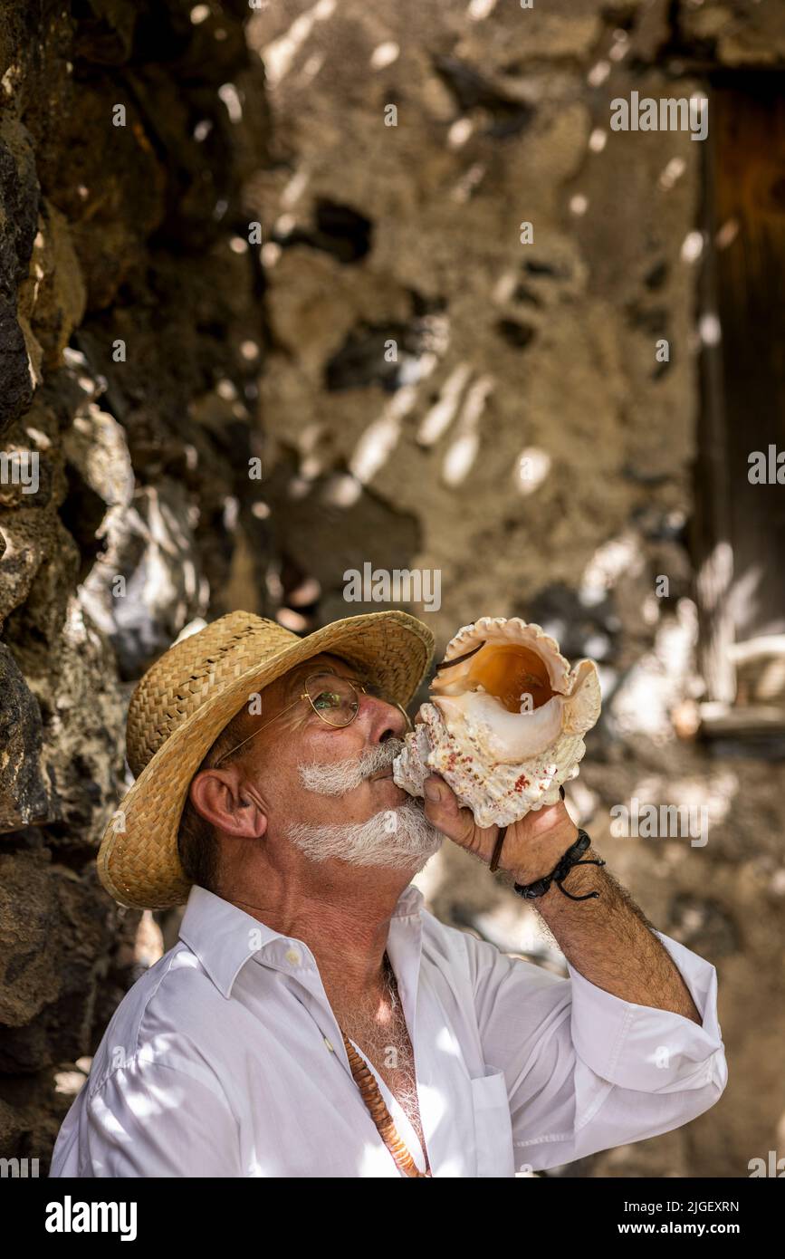 Chirche, Tenerife, 10 July 2022. A man blows into a conch to draw peoples attention. Villagers celebrate the Día de tradiciones, Day of Traditions in the small mountain village where they renact scenes from the rural lifestyle lived by their ancestors in the 1940s Stock Photo