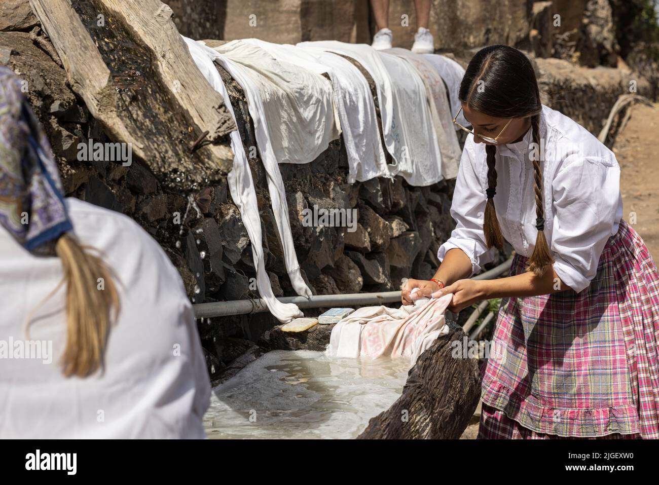 Chirche, Tenerife, 10 July 2022. Young girls washing clothes in a wooden trough at the communal wash place. Villagers celebrate the Día de tradiciones, Day of Traditions in the small mountain village where they renact scenes from the rural lifestyle lived by their ancestors in the 1940s Stock Photo