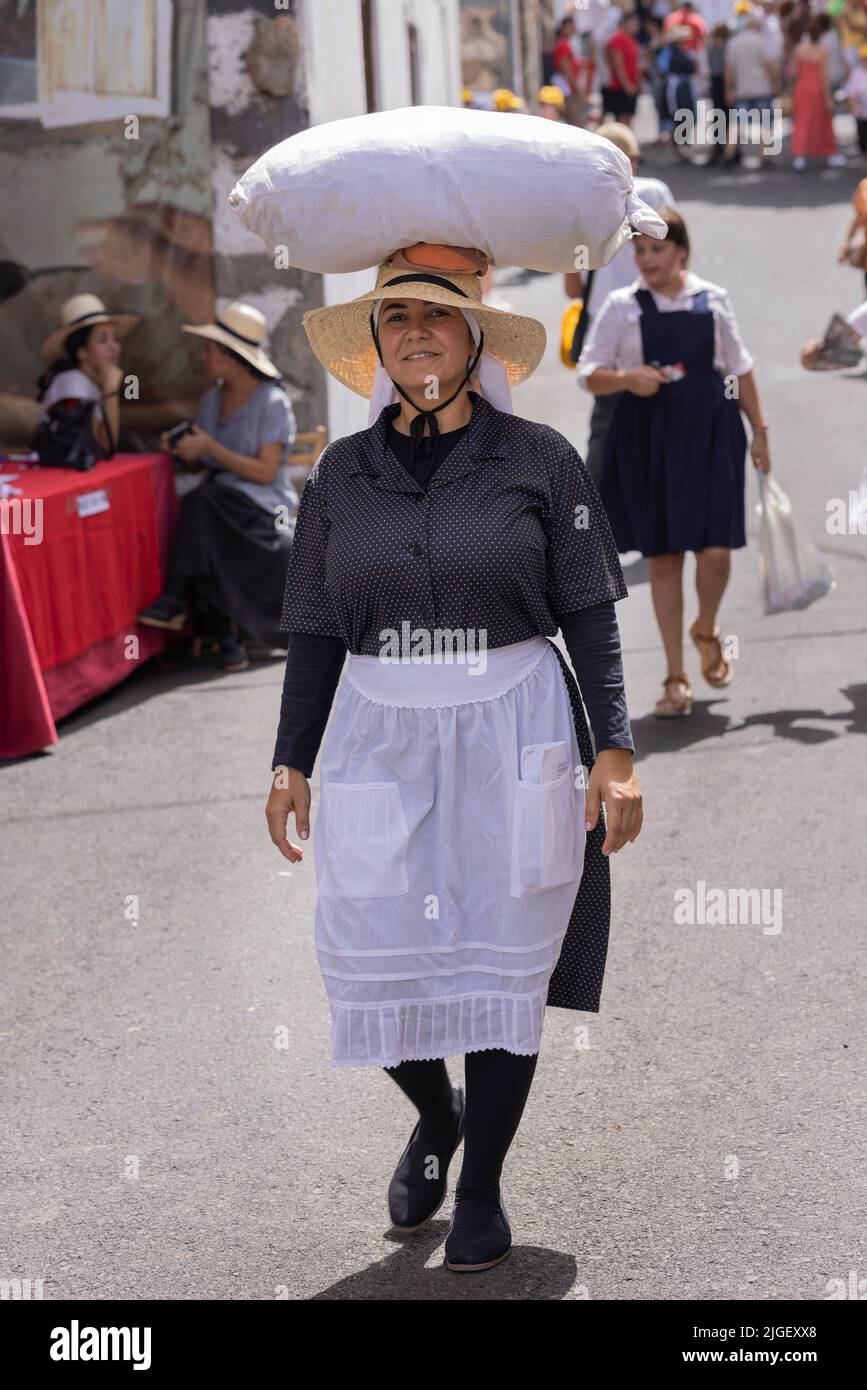 Chirche, Tenerife, 10 July 2022. A woman carries a sack of goods on her head as she walks down the street. Villagers celebrate the Día de tradiciones, Day of Traditions in the small mountain village where they renact scenes from the rural lifestyle lived by their ancestors in the 1940s Stock Photo