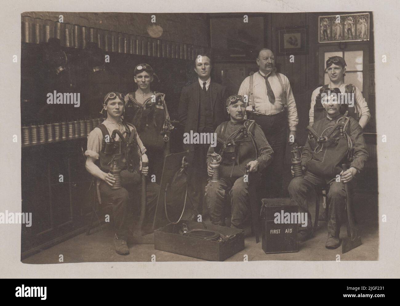 Early 20th century mine rescue team in South Wales. The men are dressed in rescue equipment with breathing apparatus, lamps, goggles, axes, a saw and a first aid kit. Rows of mining lamps are lined up in the background. The photograph was published as a postcard by Chapman of Swansea Stock Photo