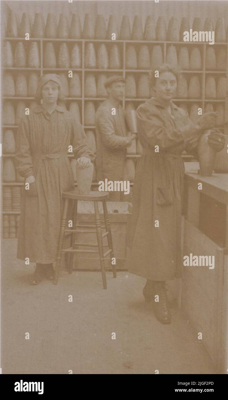 First World War munitions workers in a British factory. Photograph of two women and a man at work, rows of shells are lined up on shelves in the background Stock Photo