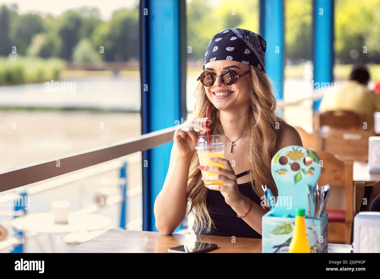 Hipster beautiful woman with head scarf and retro sunglasses drinking fresh lemonade juice at restaurant Stock Photo
