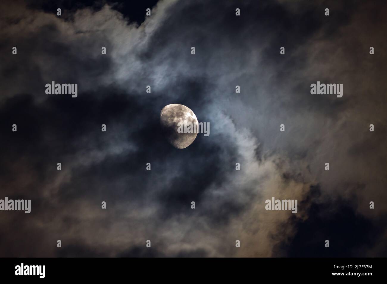 A three-quarter, waxing gibbous moon illuminates passing turbulent clouds in a night sky. Stock Photo