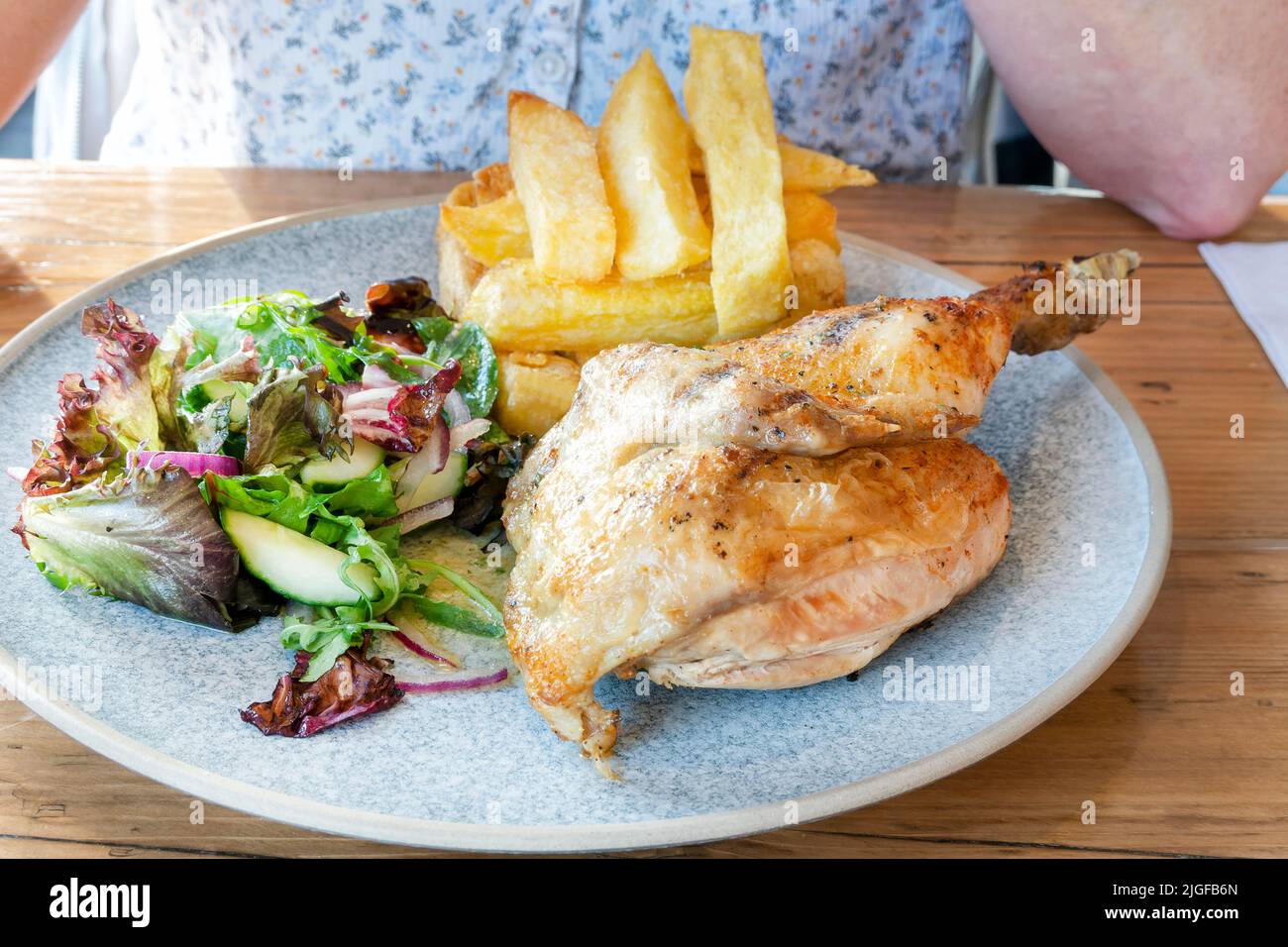 A traditional British half roast chicken pub meal. The meat has been served to the table with a stack of triple cooked chunky chips and a mixed salad. Stock Photo