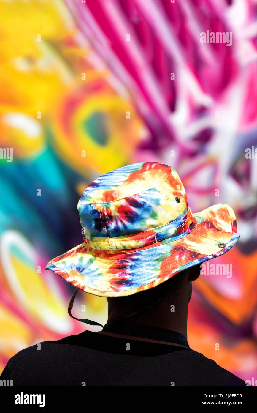 Bristol, UK. 28th May 2022. A street artist wearing a colourful, tied dyed hat stands back to access his artwork during the Bristol Upfest, 2022, fest Stock Photo