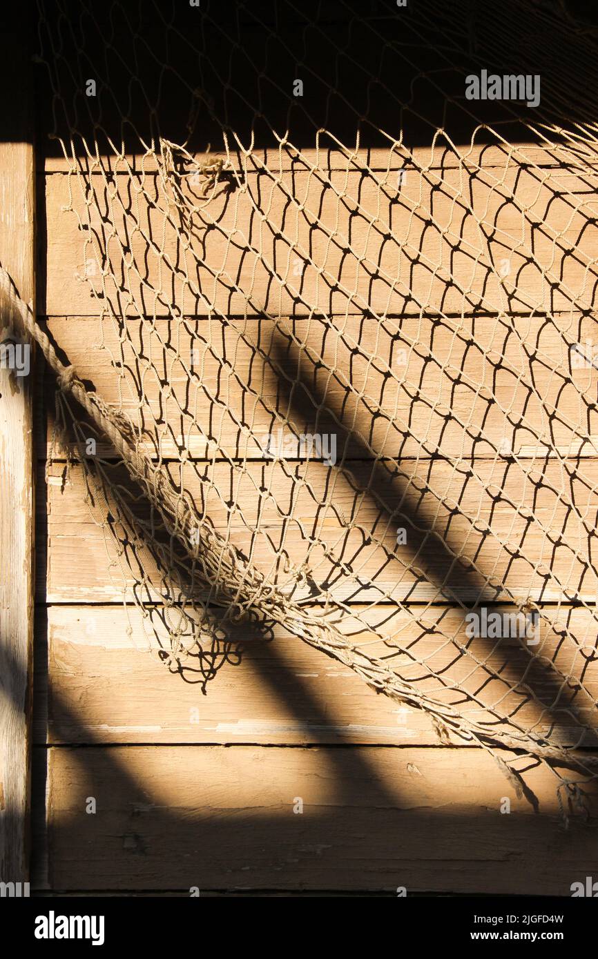 Fishing net at the fisherman's house. Fishnet hanging on the wooden wall. Abstract sea life background. Stock Photo