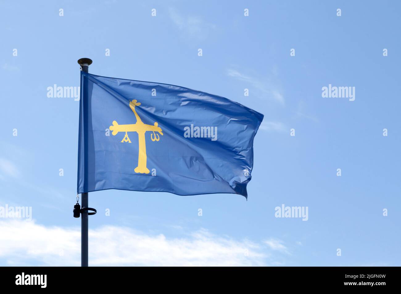Flag of Asturias (Victory Cross) waving atop of its pole against a blue sky. Stock Photo
