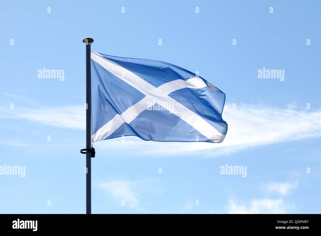 Scottish Saltire flag (St. Andrew's Cross) waving atop of its pole against a blue sky Stock 
