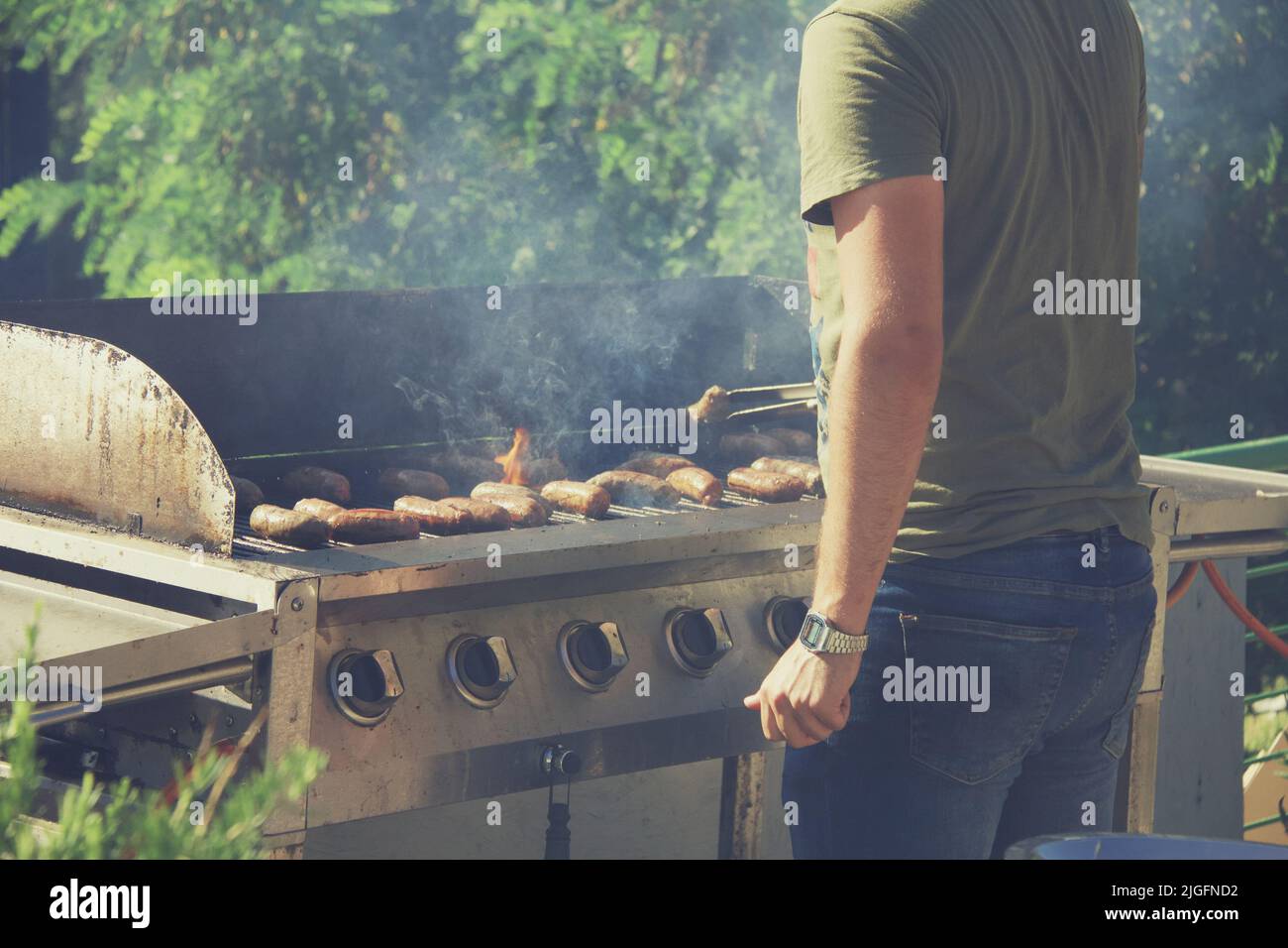 Guy cooking sausages on barbecue grill, open fire on a summer day in