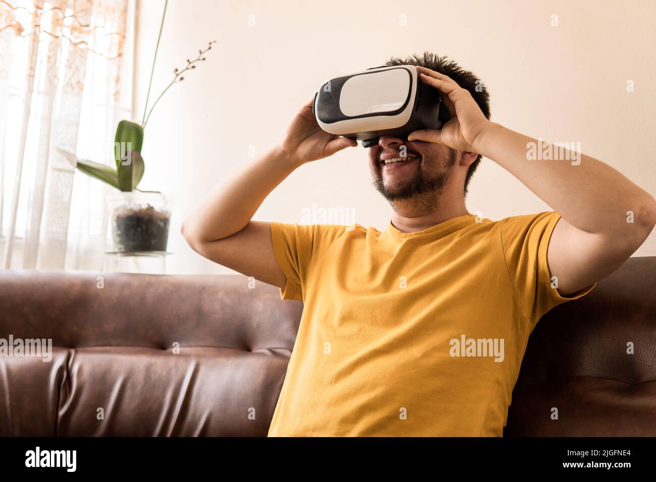 A Latin mid-adult man is wearing a VR Headset and he is sitting on the sofa Stock Photo