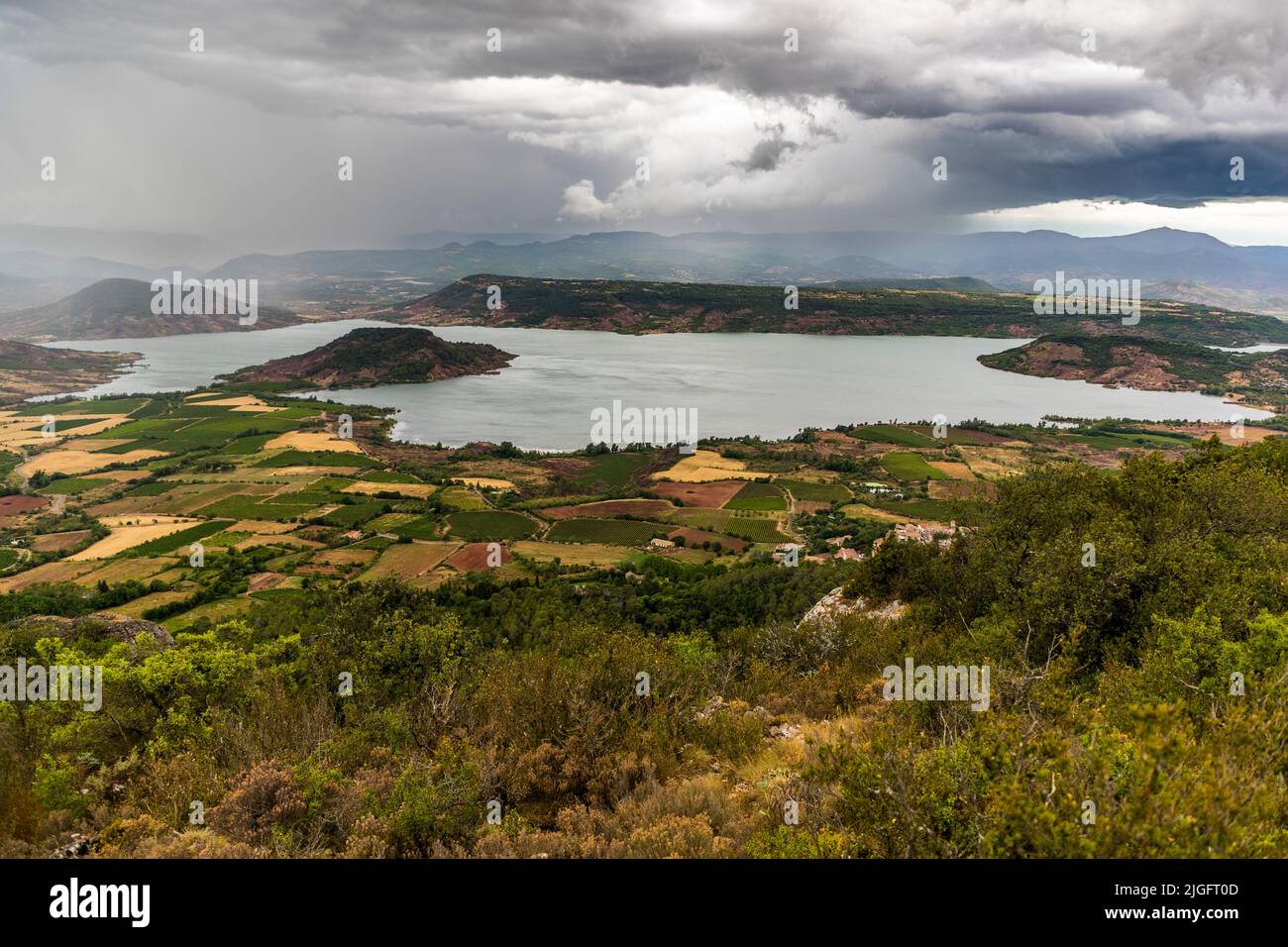 The Salagou reservoir north of Mourèze, Hérault, France, lies beneath an approaching storm sky. The lake was created in the 1960s to supply the valley with water. The area's characteristic red soil, known as ruffes, colours the surrounding fields. Stock Photo