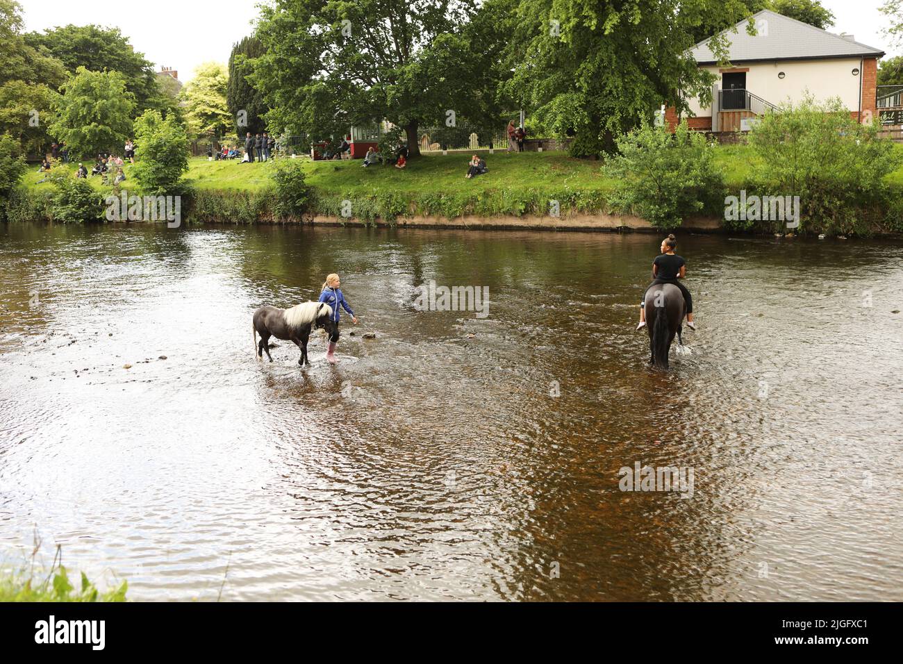 A young woman riding her horse in the River Eden, a young girl leading a grey pony, Appleby Horse Fair, Appleby in Westmorland, Cumbria Stock Photo