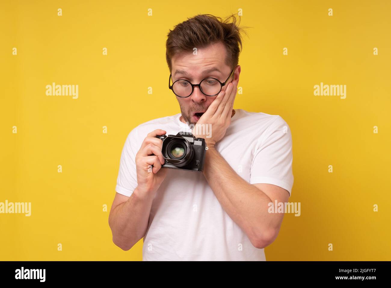Young photographer caucasian man being surprised and shocked looking at camera Stock Photo