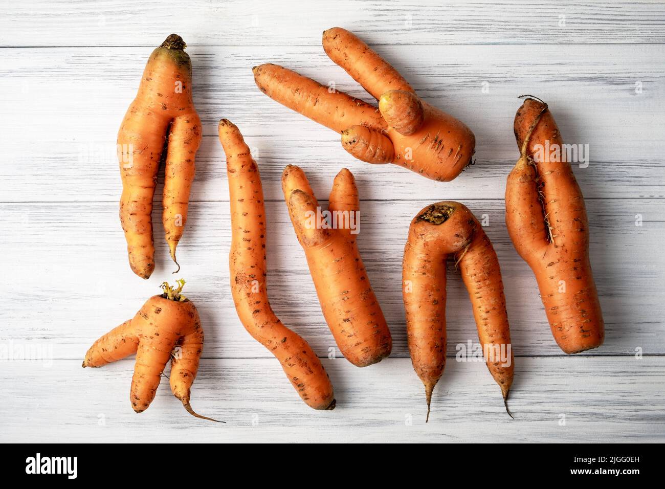 Several ripe orange ugly carrots lie on a light wooden surface. Selective focus. Stock Photo