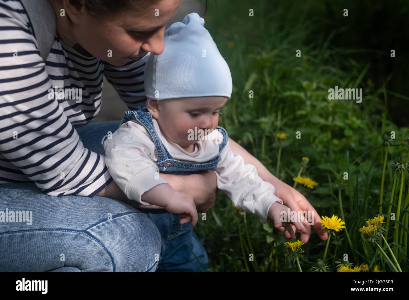 Summertime. A mother holds her baby in her arms and shows him a flower in the backyard. Stock Photo