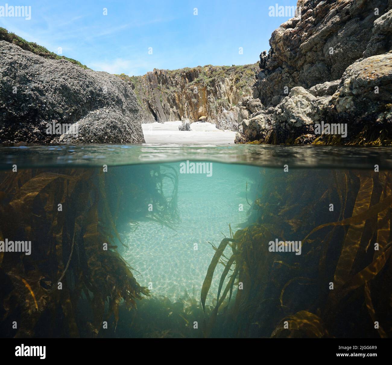 Narrow passage between rocks to a secluded beach with kelp underwater, split level view over and under water surface, Atlantic ocean, Spain, Galicia Stock Photo