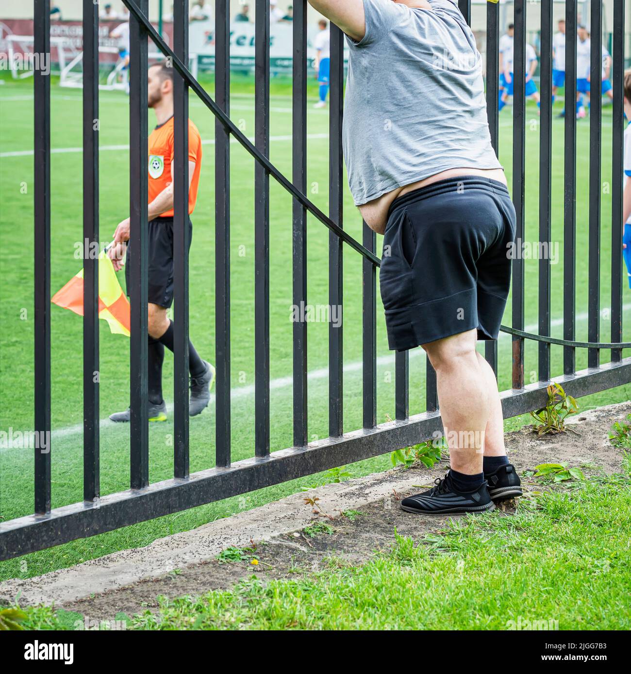 Fat man, fan looks behind fence at sports game, football. Sport, diet