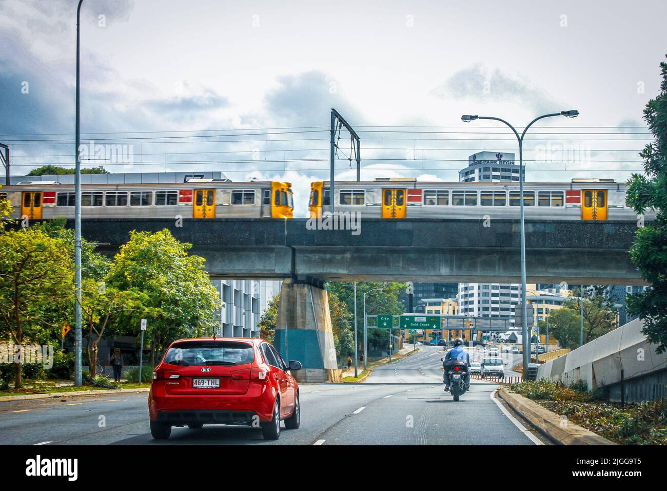 2014 12 04 Brisbane Australia - Red car and motorcycle drive under overpass with train distant sign for exit to Gold Coast and City Stock Photo