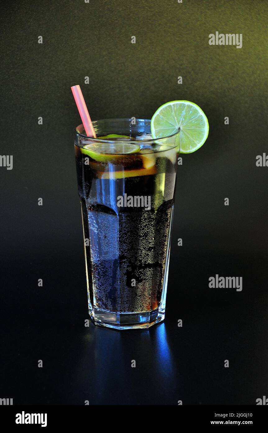 Cola with lime, a refreshing drink in a tall glass with ice and straws ...