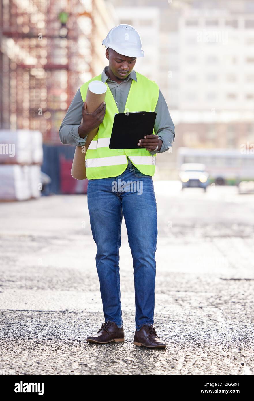 Keeping an eye on the process. Full length shot of a handsome young construction worker standing with blueprints and clipboard on a building site. Stock Photo