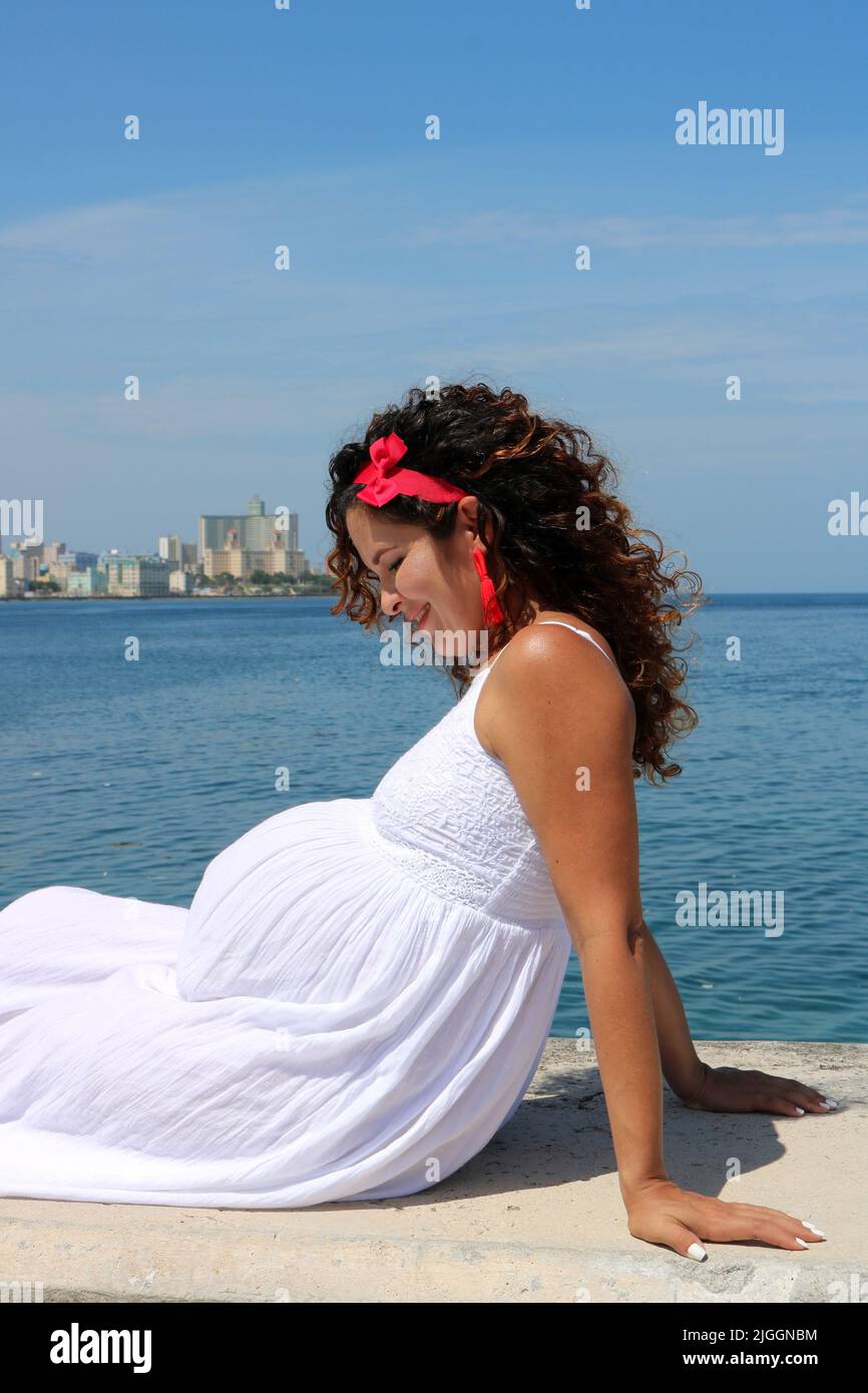 Profile view of eight-month pregnant woman with ocean and city behind Stock Photo