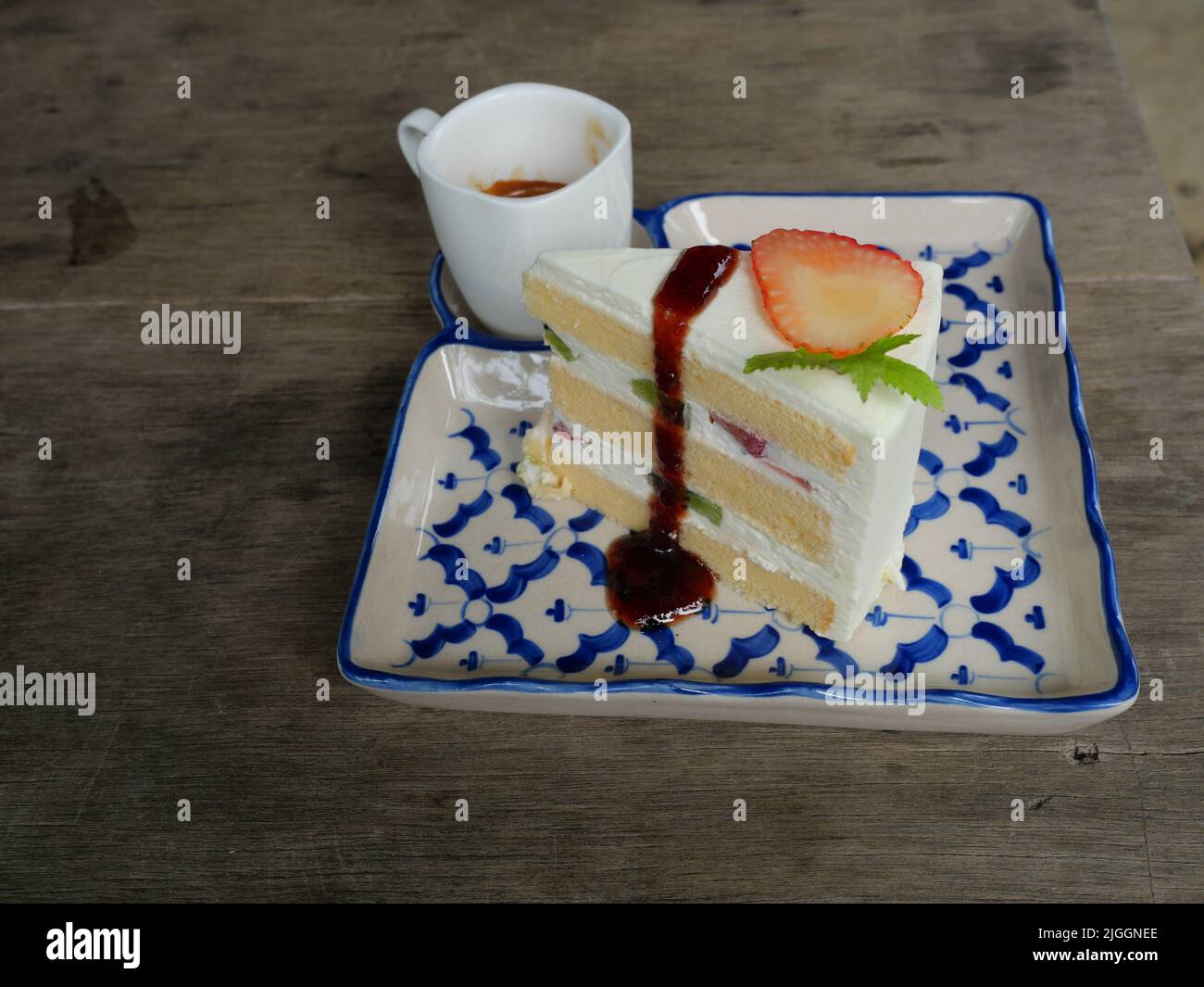 Strawberry and kiwi fruit slice with red color syrup and cream sponge cake in a ceramic tray on gray wood table, Hot espresso coffee in white cup Stock Photo