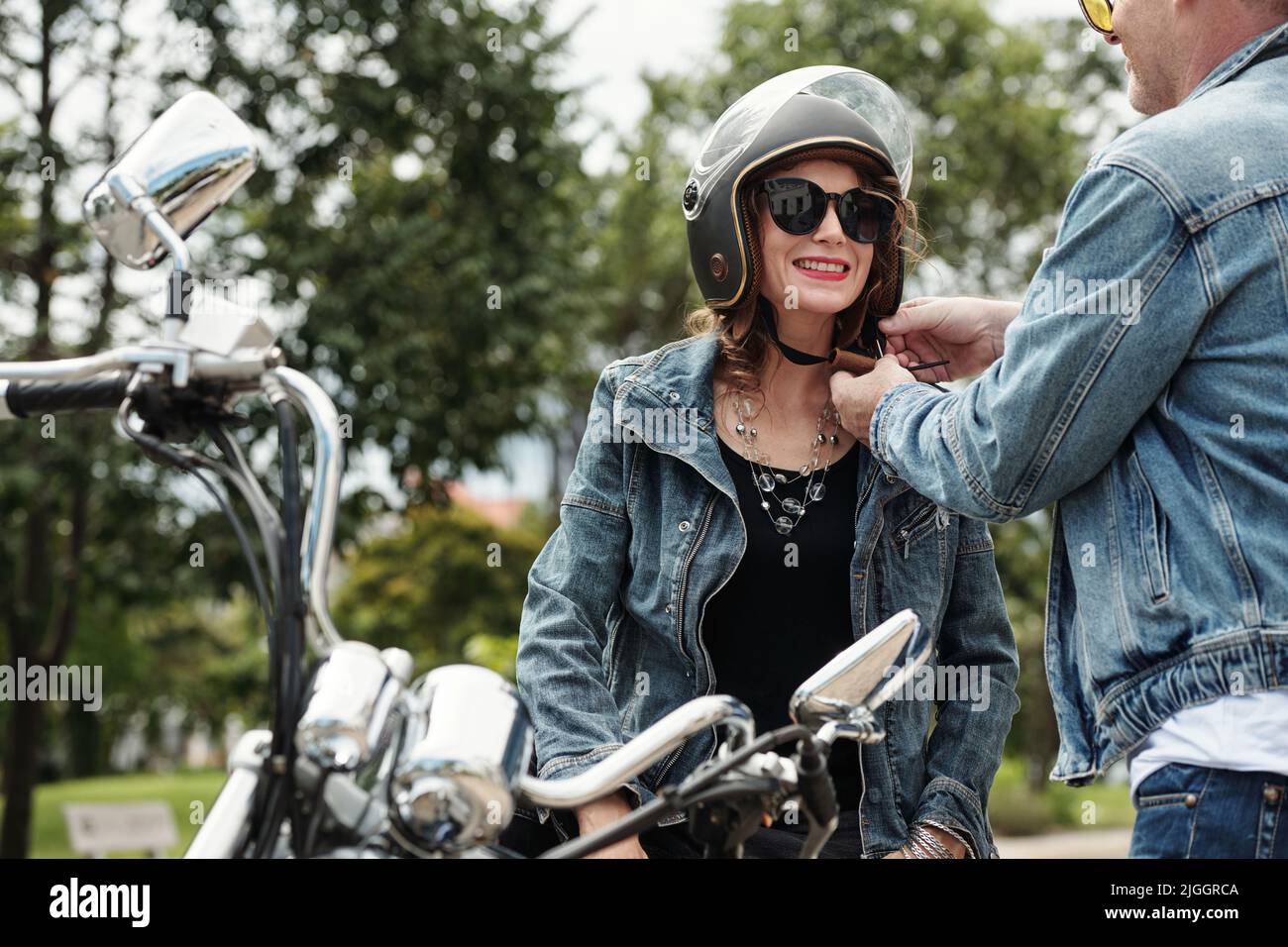 Caring man helping girlfriend to take on motorcycle helmet before ride
