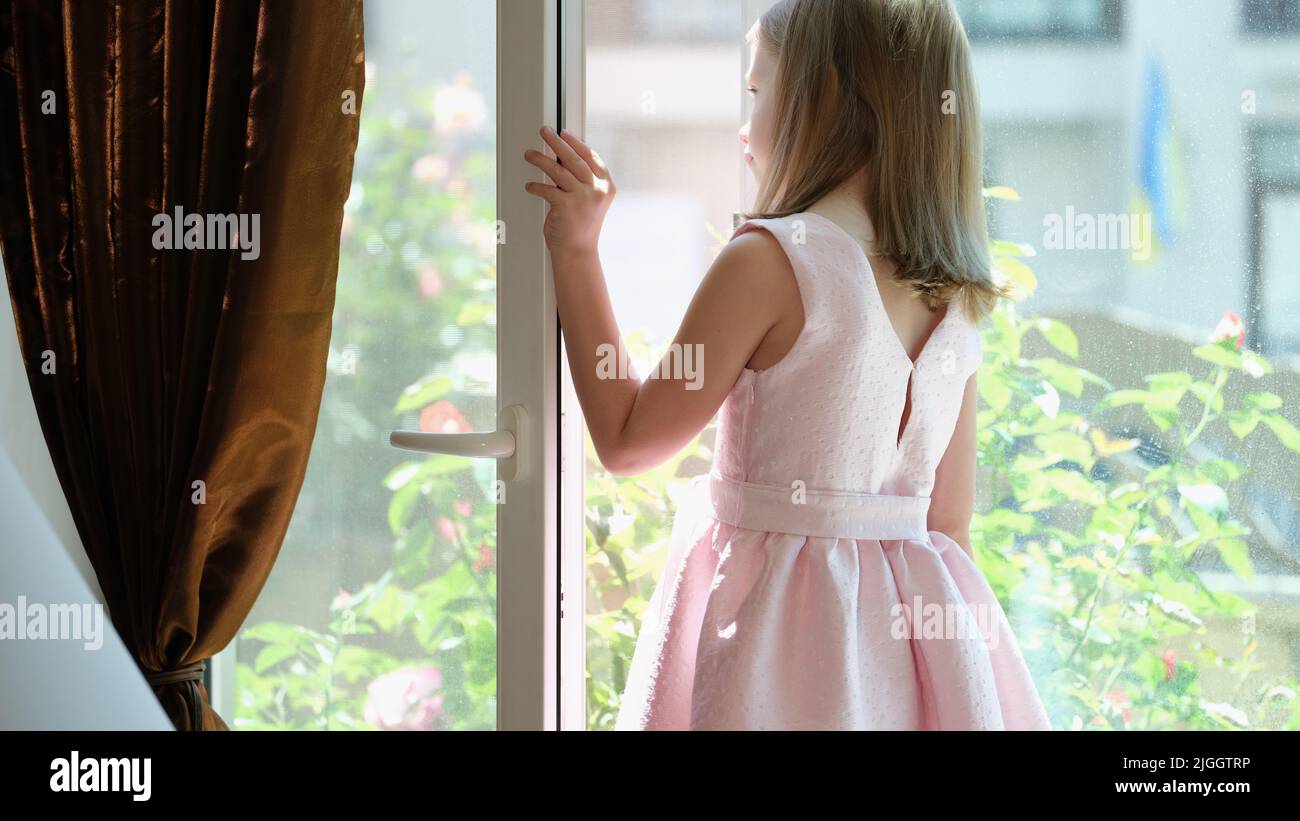 Little girl in pink dress standing on windowsill at open window Stock Photo