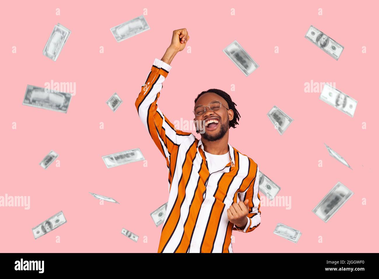 Money rain, winner and rich. Hurray. satisfied happy young man rising hands up with toothy smile on face, pleased, amazed with money falling. Indoor studio shot isolated on pink background Stock Photo